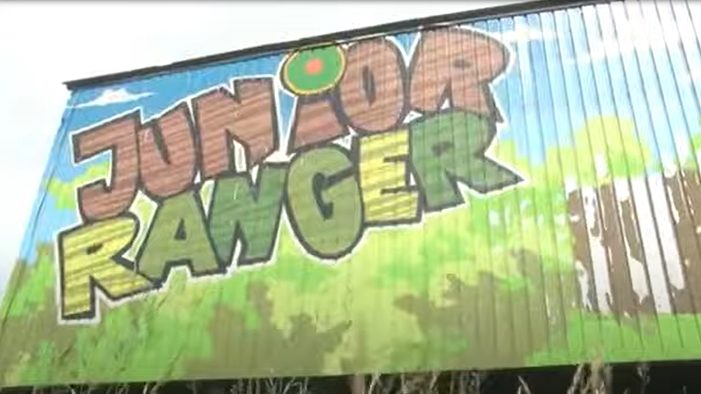 Die Aufnahme zeigt das Abenteuer Junior Ranger. Auf dem Bild liegt ein Play-Button zum Aktivieren des Videos