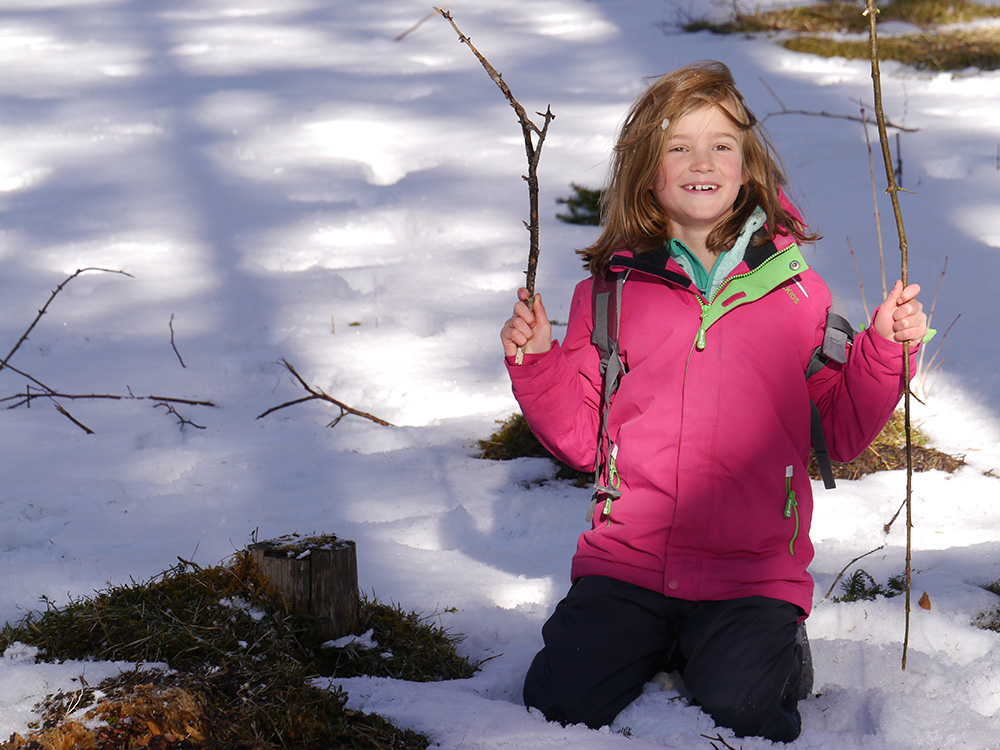 Kind im Schnee mit Ästen in der Hand